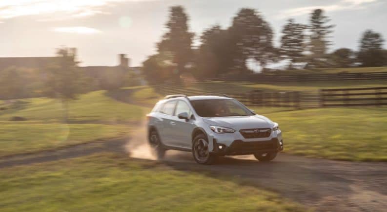 A white 2021 Subaru Crosstrek is driving on a dirt road past a fence.