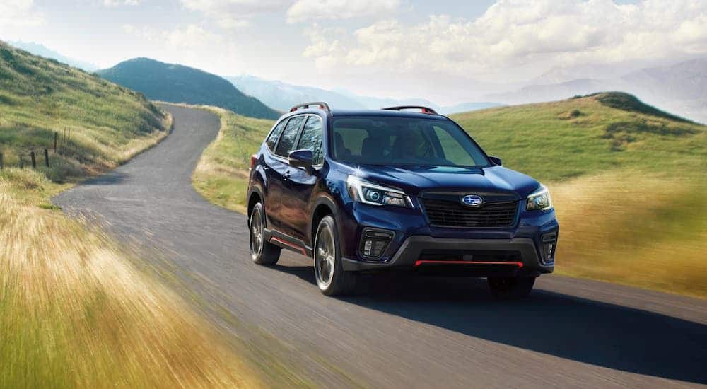 A dark blue 2021 Subaru Forester is driving on an empty road through hills.