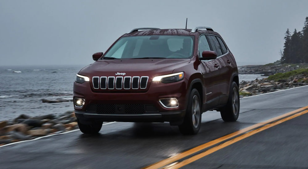 A maroon 2021 Jeep Cherokee is driving past a lake.