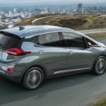 A used grey 2020 Chevy Bolt EV is driving past a city after searching for used car dealers near me.