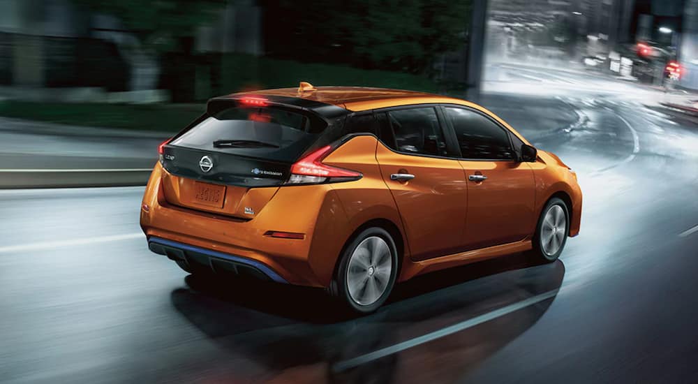 A used orange 2020 Nissan LEAF is driving through a city at night.