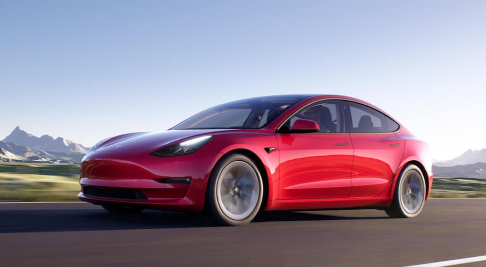 A red 2020 Tesla Model 3 is driving down an open road.