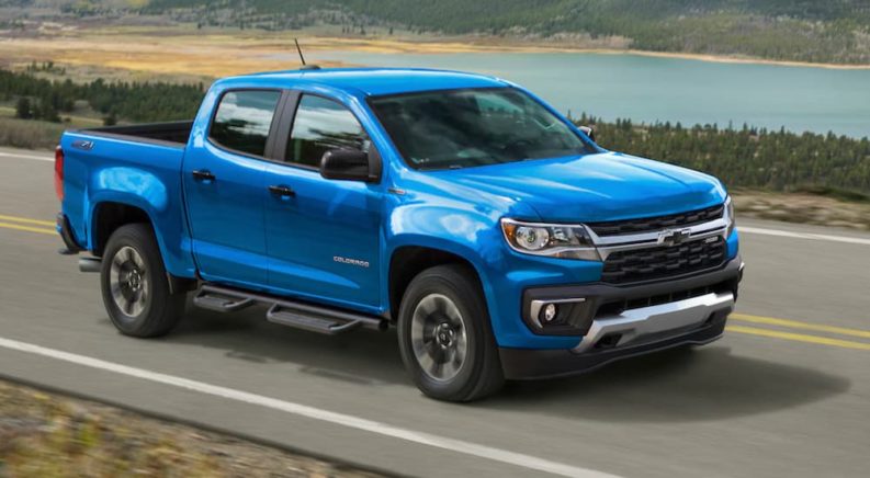 A light blue 2021 Chevy Colorado is driving down an open road in front of a pond.