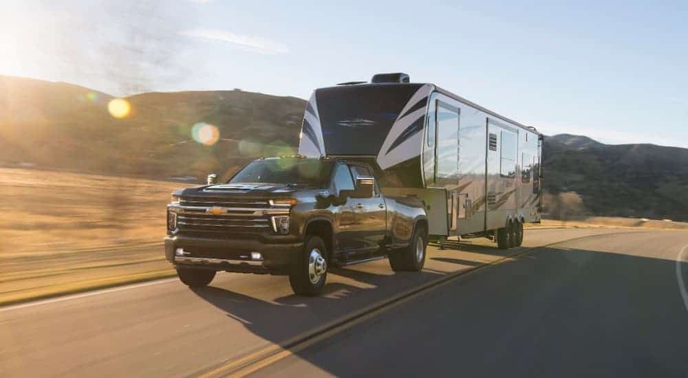 A black 2021 Chevy Silverado 3500 HD is towing a large camper on a rural road.