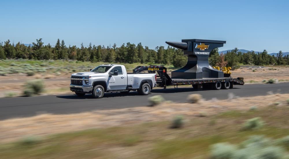 A white 2021 Chevy Silverado 3500 HD is towing a giant anvil on a rural road.