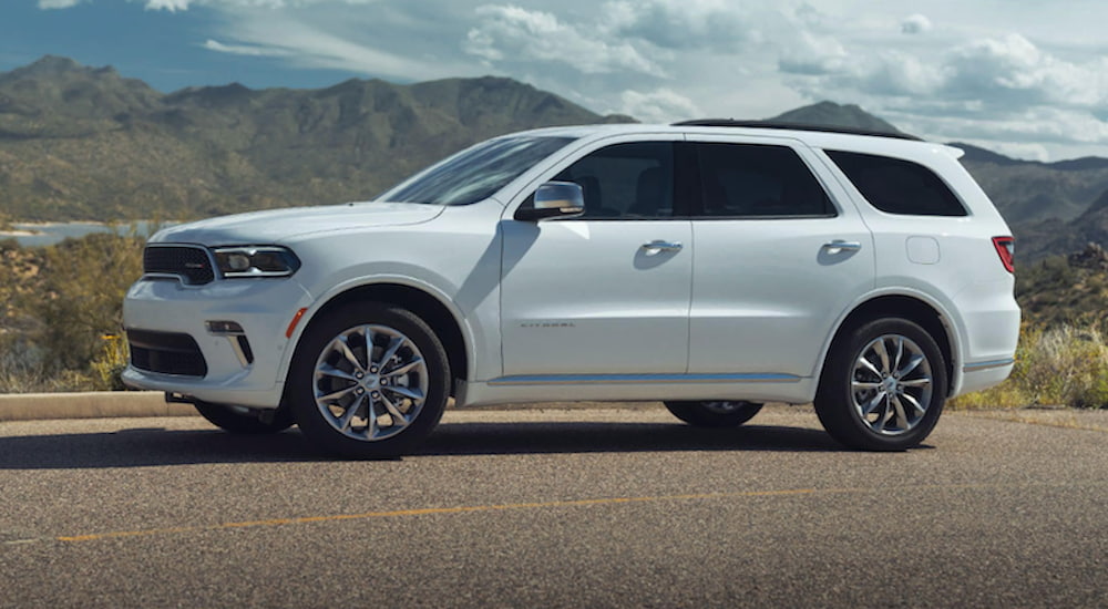A white 2021 Dodge Durango is driving on an open road in front of mountains.