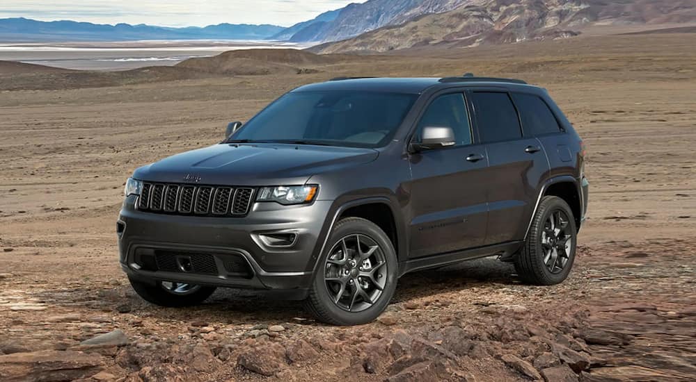 A dark grey 2021 Jeep Grand Cherokee is parked in a field in front of mountains. 