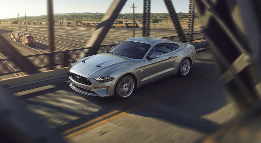 A silver 2021 Ford Mustang is shown from an angle driving over a bridge.