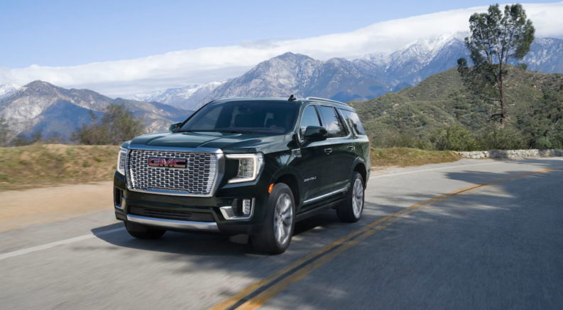 A black 2021 GMC Yukon Denali is driving on a two way road past mountains.