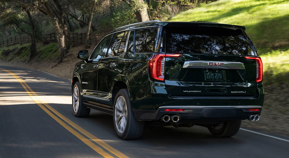 a black 2021 GMC Yukon Denali is shown from the rear as it drives down a two way road. 