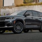 A black 2021 Jeep Grand Cherokee L is parked outside of a house during the day.