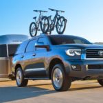 A grey 2021 Toyota Sequoia with bikes on the roof is towing an Airstream past rolling hills.