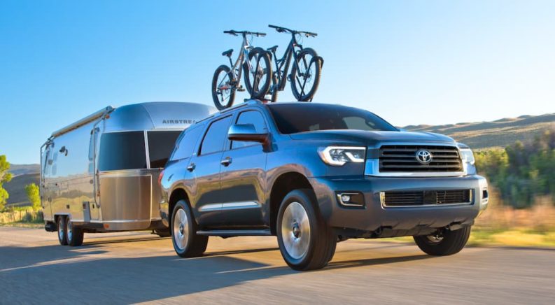 A grey 2021 Toyota Sequoia with bikes on the roof is towing an Airstream past rolling hills.