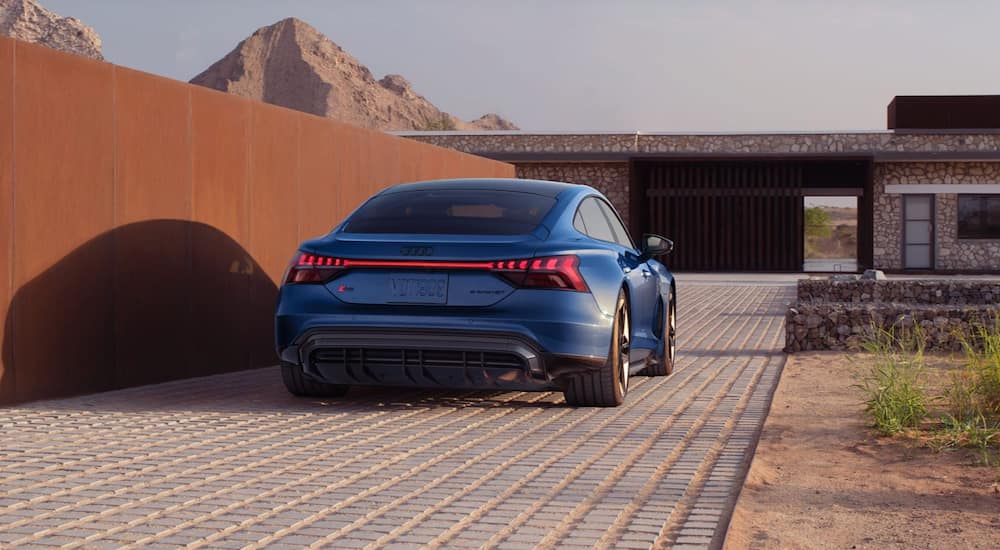A blue 2022 Audi e-Tron GT is shown from the back parked outside of a modern building. 