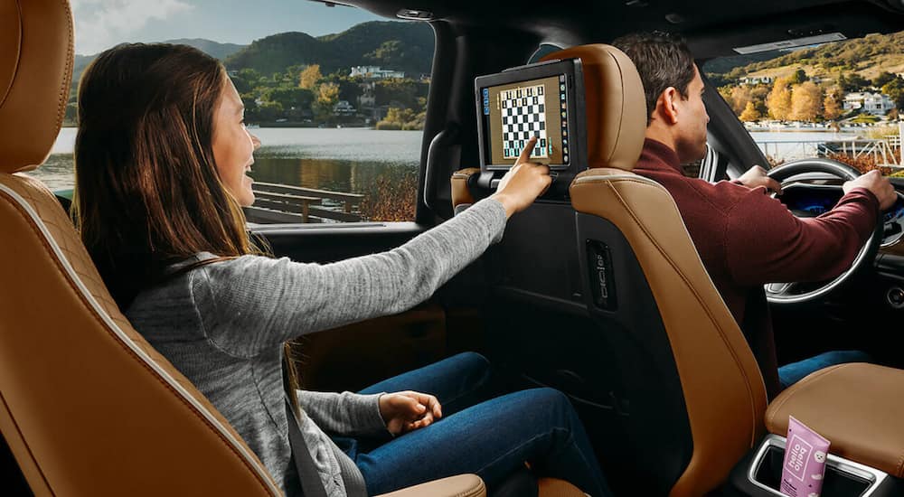 The interior of a 2021 Chrysler Pacifica shows a child in the back seat playing a game on an infotainment screen.