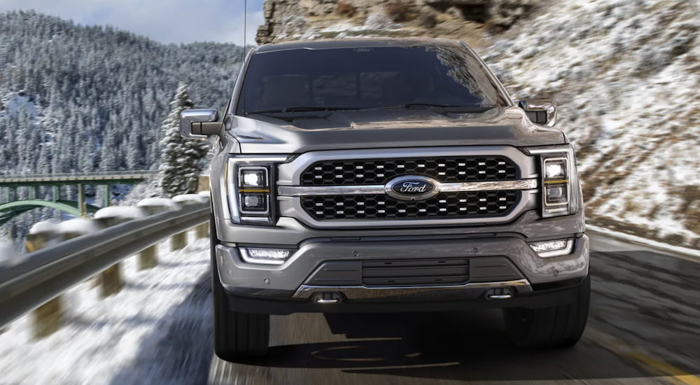 A silver 2021 Ford F-150 is shown from the front driving on a two way road in the mountains.