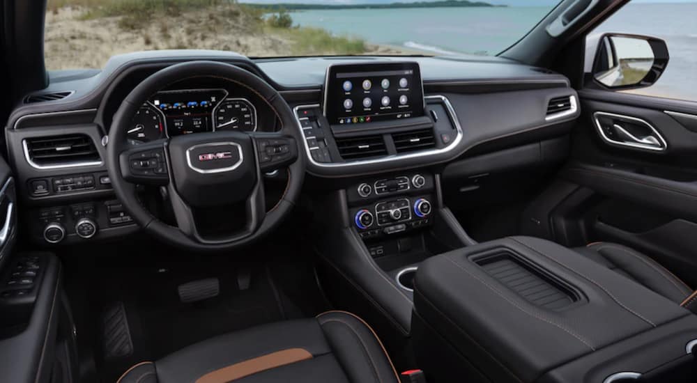 The black interior of a 2021 GMC Yukon AT4 shows the steering wheel and infotainment screen.
