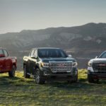 A red, a black, and a white 2021 GMC Canyon are parked in a field with mountain views.