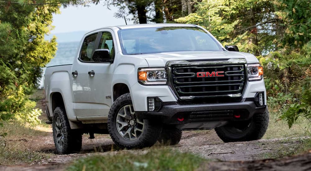 A white 2021 GMC Canyon from a new truck dealership is on a dirt path in the woods.