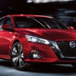 A red 2021 Nissan Altima is driving through a city at night.