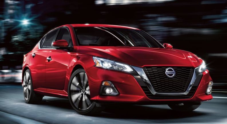 A red 2021 Nissan Altima is driving through a city at night.