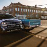 A blue 2018 Chevy Silverado 1500 from a used Chevy truck dealer is passing a blue 1972 C10 on a downtown street.