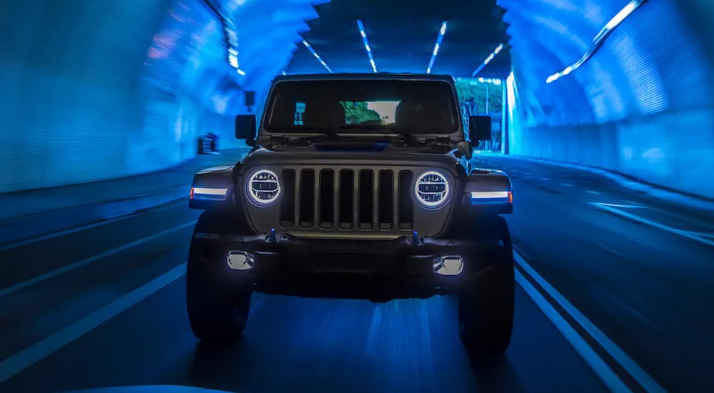 The front of a 2021 Jeep Wrangler 4xe is shown driving through a tunnel with blue light.