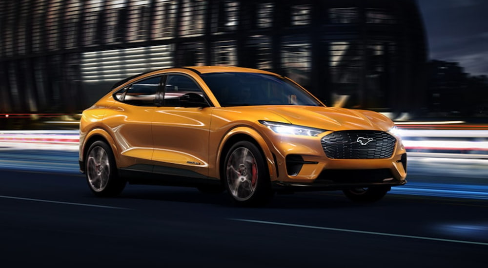 A yellow 2021 Ford Mustang Mach-E is driving through a city at night.