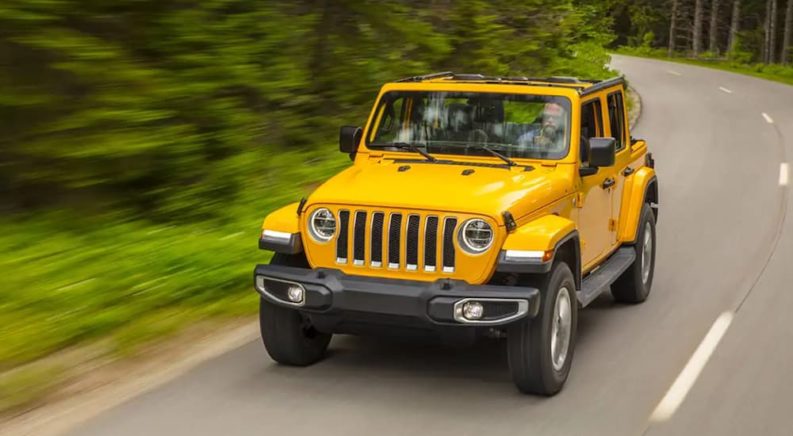 A yellow 2021 Jeep Wrangler is driving down a winding road after leaving a used Jeep dealer