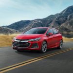 A red 2019 Chevy Cruze is driving down an open road in front of a mountain.