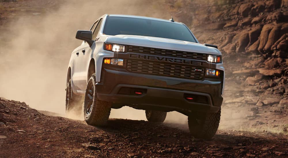 A white 2021 Chevy Silverado 1500 is shown from the front driving through a desert after the owner searched 'sell my car'.