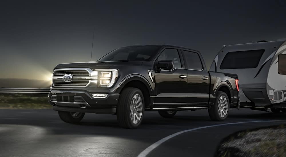 A black 2021 Ford F-150 is towing a trailer at night.