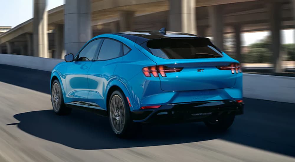 A blue 2021 Ford Mustang Mach-E is shown from the back driving onto a highway ramp.