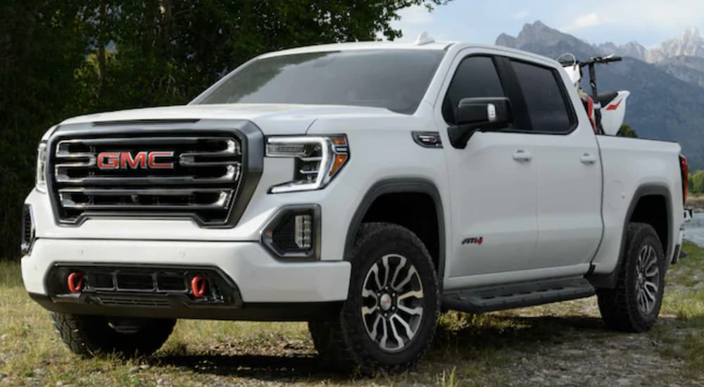 A white 2021 GMC Sierra 1500 is parked in a grass field in front of mountains.
