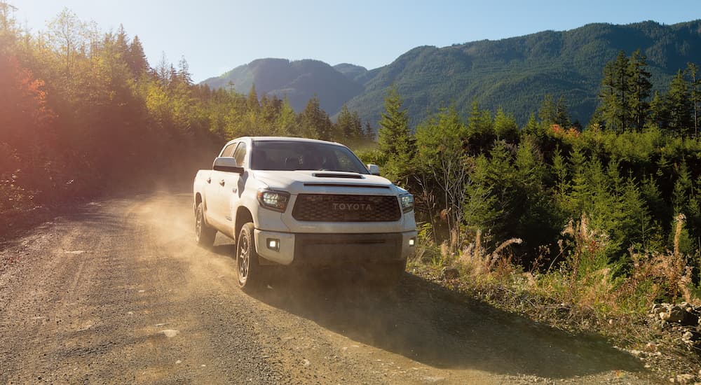 A white 2021 Toyota Tundra is driving down a dirt road in the mountains.