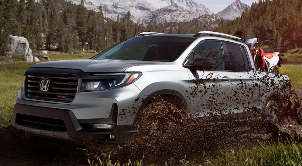 A silver 2021 Honda Ridgeline Sport is driving through a mud puddle.