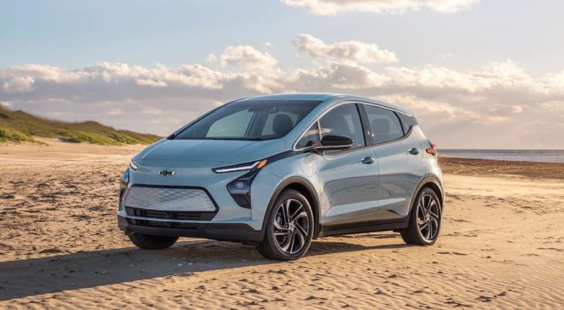 A light blue 2022 Chevy Bolt EV is shown from the side parked on a beach after leaving a Chevy dealer.