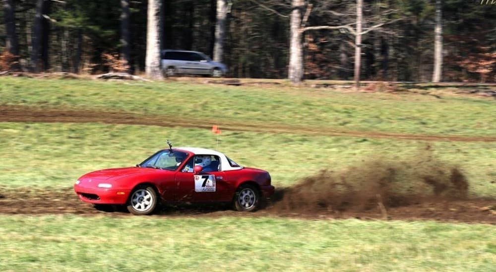 A red 1st generation Mazda Miata is shown kicking up dirt in a field.