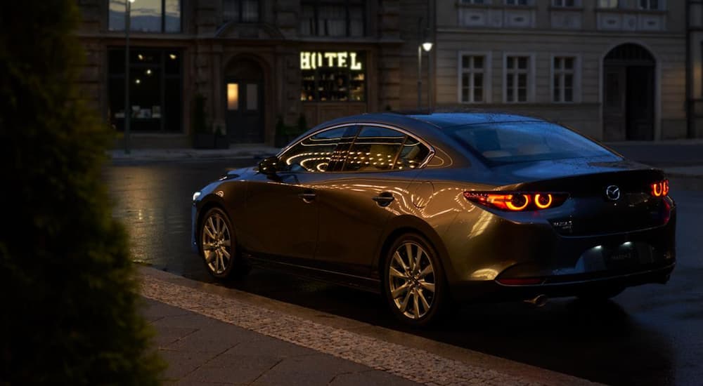 A grey 2021 Mazda3 is shown parked on a city street at night.