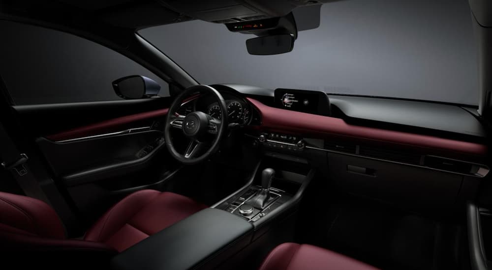 The red and black interior of a Mazda3 shows the steering wheel and front seats.