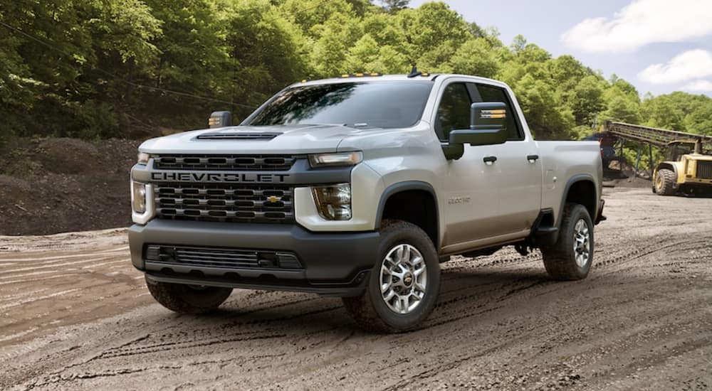 A white 2021 Chevy Silverado 2500 is parked on a dirt construction site in front of the woods.