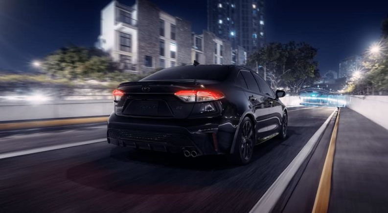 A black 2021 Toyota Corolla is driving through a city at night after leaving a Toyota Corolla dealer.
