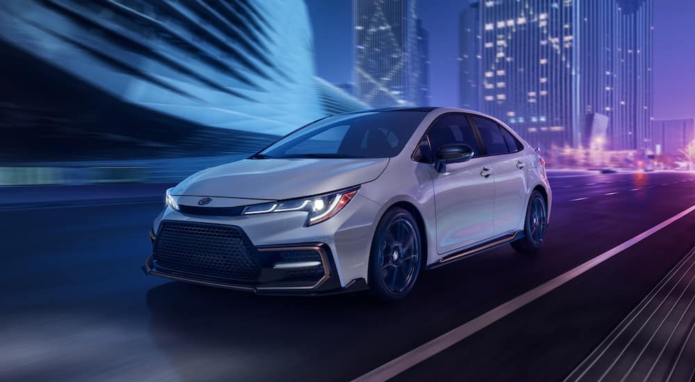 A white 2021 Toyota Corolla is driving through a city at night.
