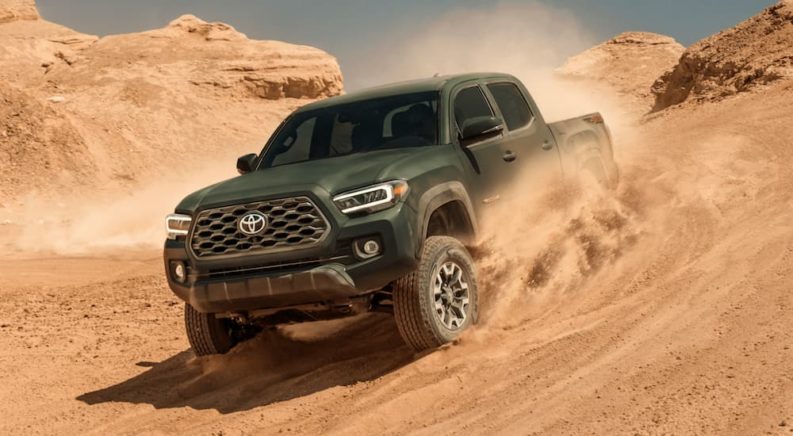 A green 2021 Toyota Tacoma is driving down a hill in a desert after leaving a Toyota Tacoma dealer.