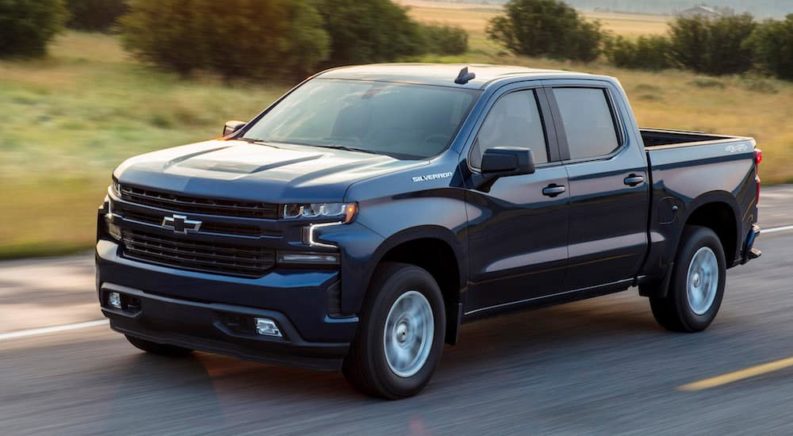 A blue 2019 Chevy Silverado is driving down a two lane road after searching used Silverado sales.
