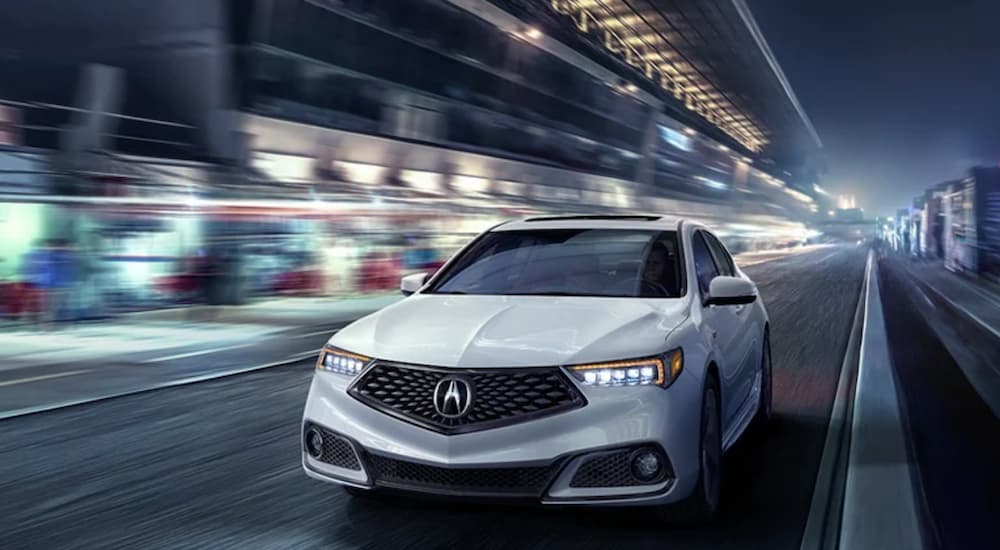 A white 2020 Acura TLX is shown driving through a city at night.