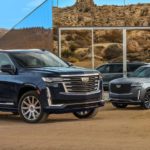 A blue and a silver 2021 Cadillac Escalade are parked in front of a modern house in the desert.