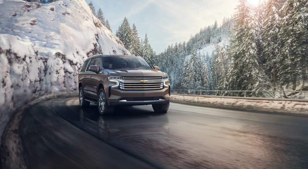 A grey 2021 Chevy Suburban is shown driving past snowy mountains.