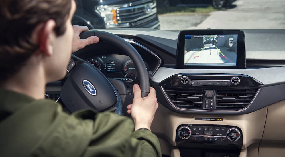 The interior of a 2021 Ford Escape Hybrid shows a man driving and taking a look at the infotainment screen.