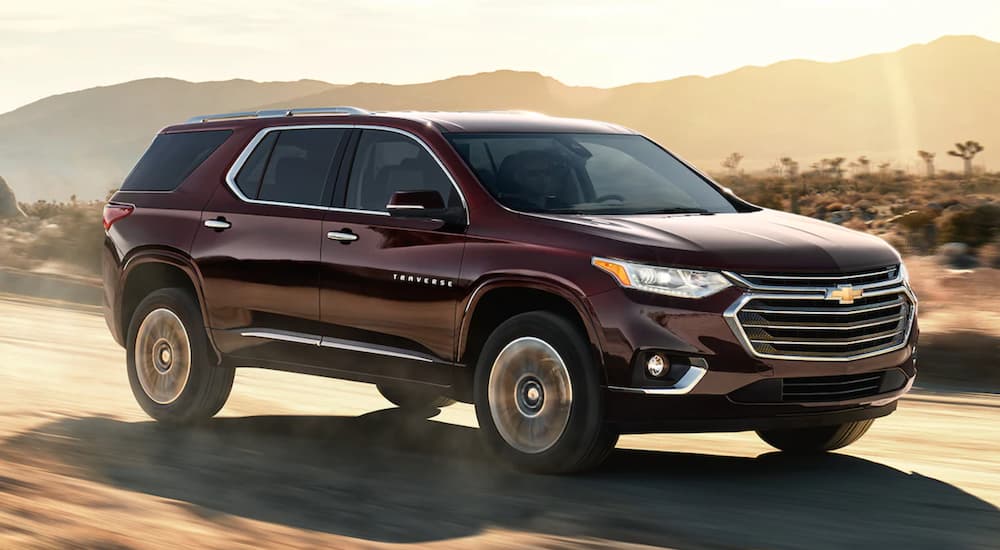 A maroon 2021 Chevy Traverse is driving on an open road through the desert.